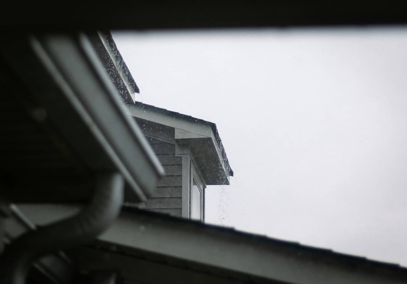 Rain running past a gutter and downspout at the eave of a gray-sided home