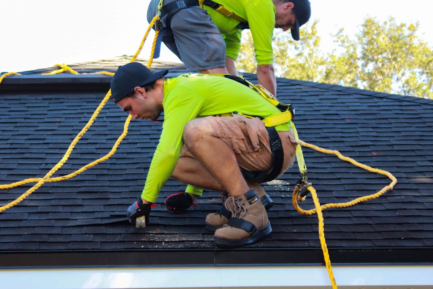 Two harnessed Watershed crew members hand-nailing architectural shingles on a steep pitch