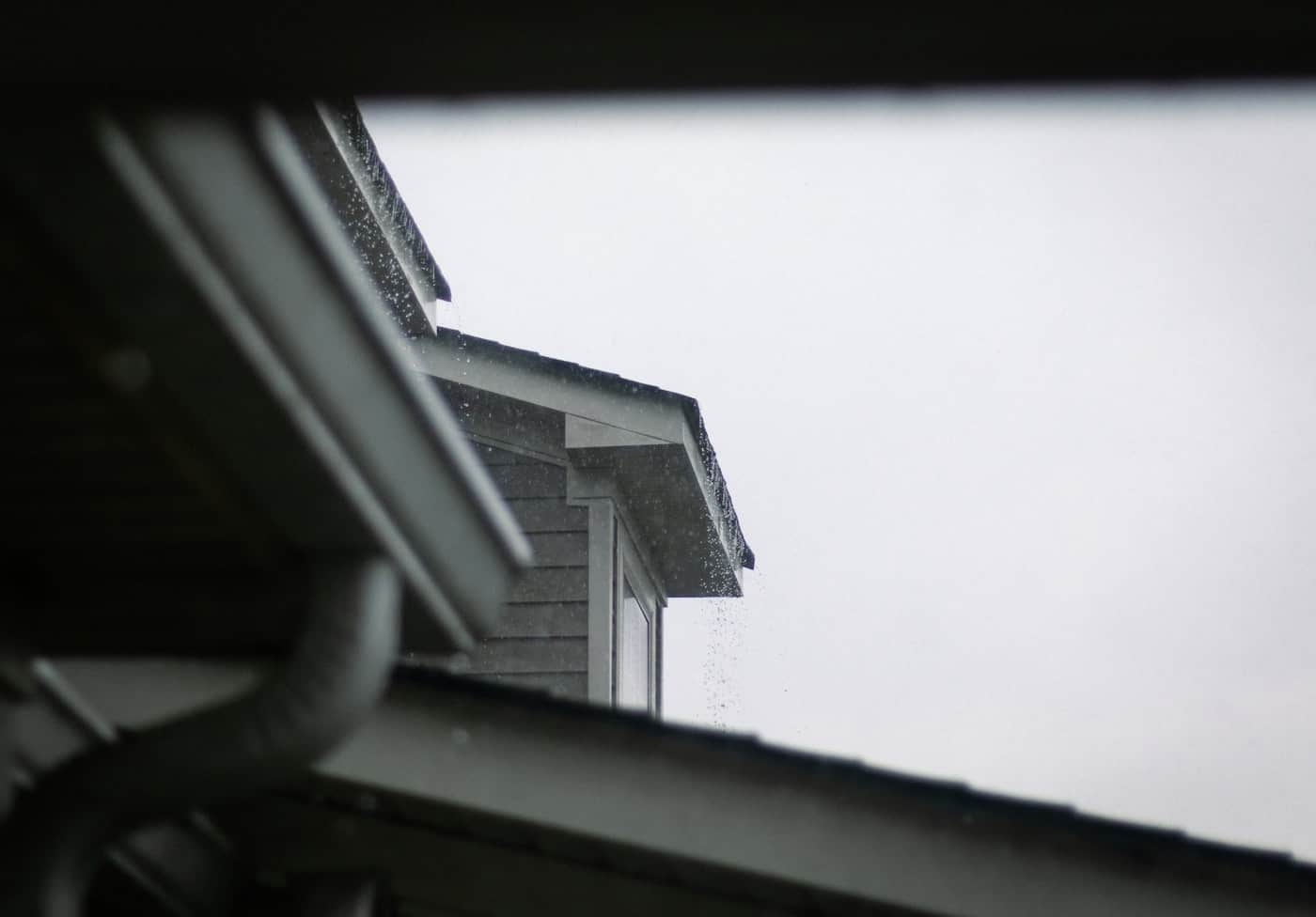 Rain running past a gutter and downspout at the eave of a gray-sided home