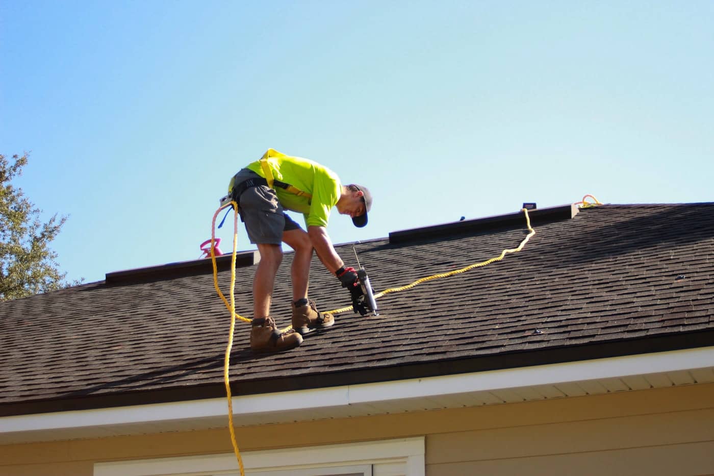 Crew member driving fasteners along a fresh course of shingles, harness line trailing behind