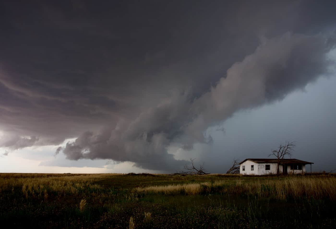 A supercell storm wall rolling over open Texas prairie toward a lone farmhouse