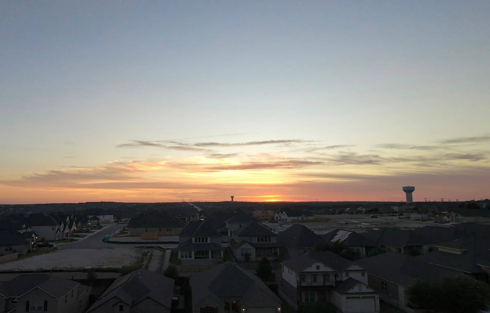 Sunset over a North Texas neighborhood, rooftops stretching to the horizon with a water tower in the distance